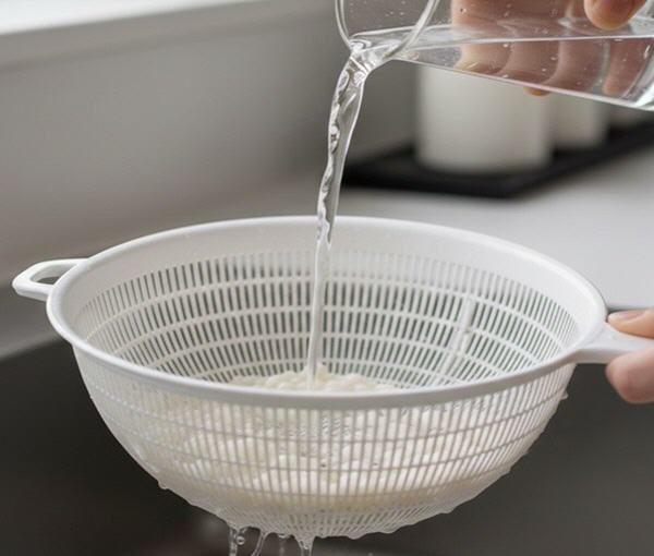 Kefirpilze in einem Sieb werden mit lauwarmen Trinkwasser abgesp&uuml;lt.